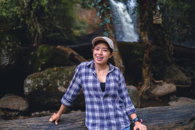 Portrait of young woman standing against waterfall