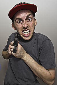 Close-up portrait of angry man holding gun while standing against gray background