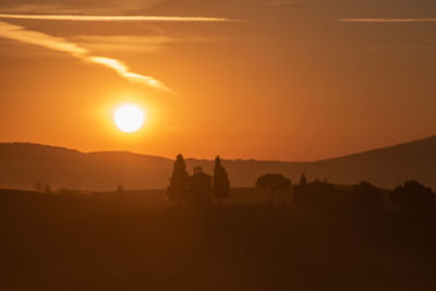 Silhouette people riding horse on field against orange sky