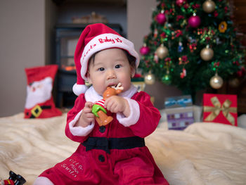 Portrait of cute baby girl wearing santa hat against christmas tree at home