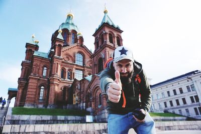 Portrait of man showing thumbs up against church