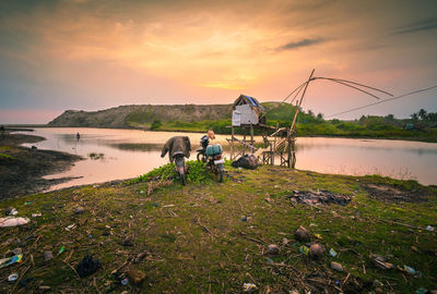 People fishing in lake against sky during sunset