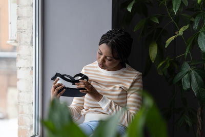 Virtual reality technology. curious black woman holding vr headset while sitting by window