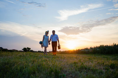 Rear view of couple on field against sky during sunset