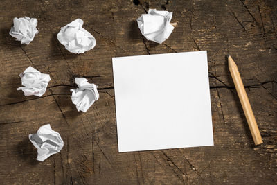 Directly above shot of crumpled balls with blank paper and pencil on wooden table