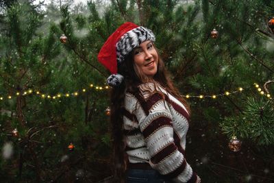 Portrait of smiling woman standing by tree during winter