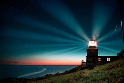 Lighthouse by sea against sky at night