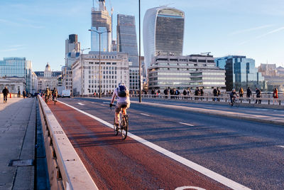 People riding bicycle on road against buildings in city