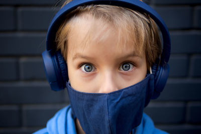 Portrait of boy wearing mask while standing against wall outdoors