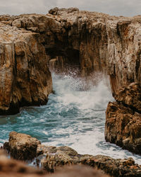 Scenic view of splashing water in sea by rock formation