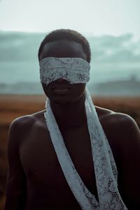 Shirtless young man with blindfold standing outdoors