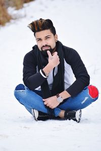 Young man sitting on snow covered land