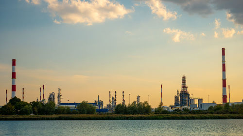 River by factory against sky during sunset