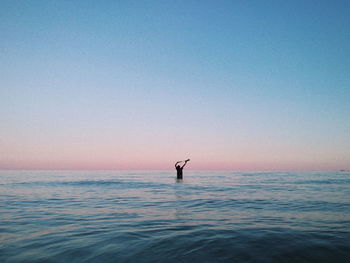 Silhouette man in sea against clear sky during sunset