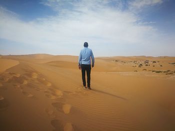 Rear view of man walking on sand dune