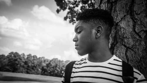 Close-up of man looking away against tree trunk