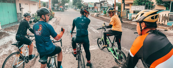 Rear view of people riding bicycle on street in city