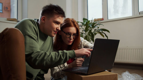 Young woman using phone while sitting on laptop