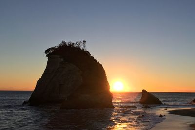 Silhouette rock in sea during sunset