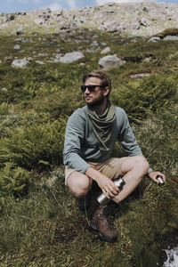 Young man wearing sunglasses sitting on land