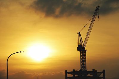 Silhouette cranes at construction site against sky during sunset