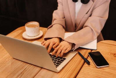 Human hands are typing on a laptop standing on a wooden table. desktop with a coffee mug