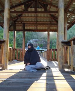 Full length portrait of woman in hijab sitting on wooden plank