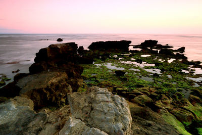 Rocks on beach against sky during sunset