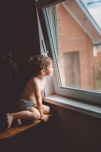 Shirtless boy looking at window at home