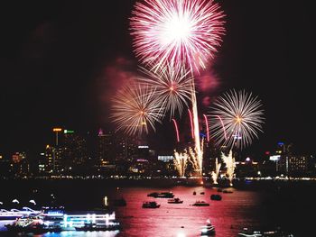 Firework display over illuminated city against sky at night