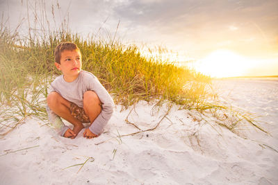 Portrait of young woman sitting on beach against sky during sunset