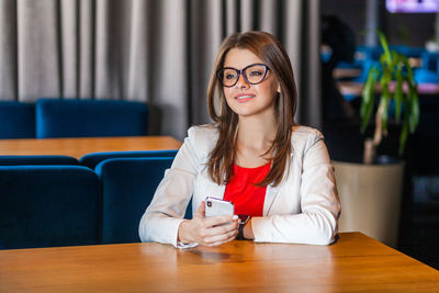 Portrait of smiling young woman using phone while sitting on table