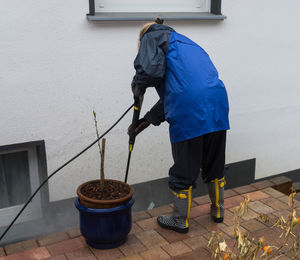 Rear view of woman working by potted plant against wall