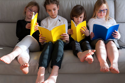 Four children sitting comfortably together on sofa in living room and doing prep work for school