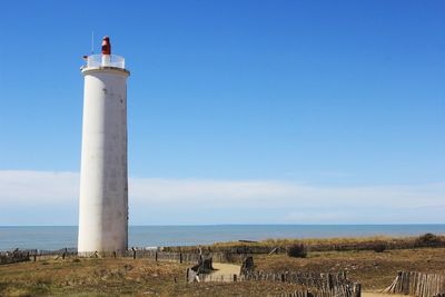 Lighthouse by sea against blue sky