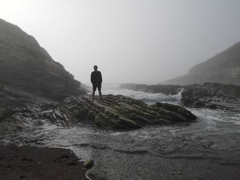 Man standing on rock by sea against sky