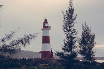 Lighthouse amidst trees and buildings against sky