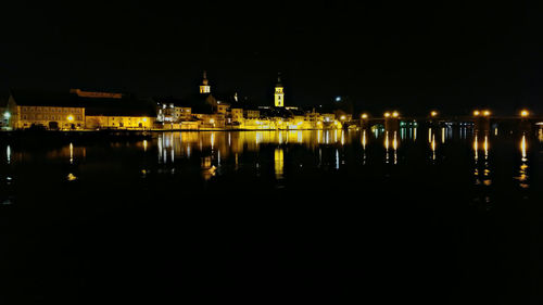 Illuminated buildings by sea against clear sky at night