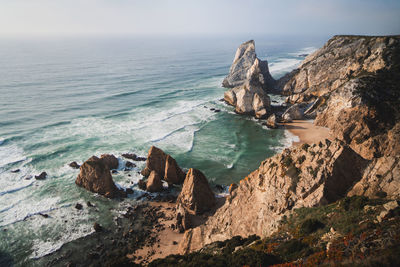 Rough rocky mountains located on sandy coast near waving sea against cloudless sky on sunny summer day in tropical resort