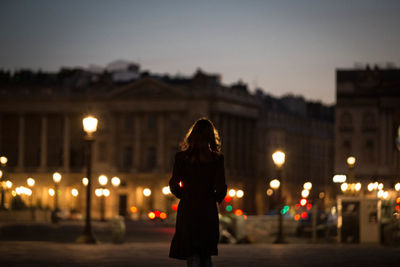 Rear view of woman standing on street in city at night