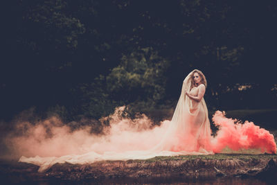 Woman standing by smoke on land against trees