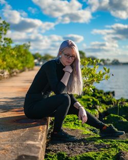 Portrait of young woman sitting on shore against sky