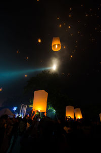 Low angle view of silhouette people with lit paper lanterns at night