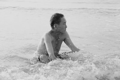 Shirtless senior man looking away while sitting on sea