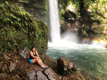 High angle view of young woman sitting on rocks against tuasan falls