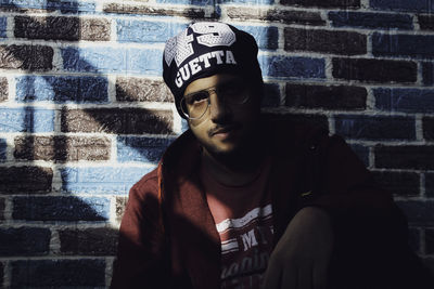 Portrait of young man standing against brick wall