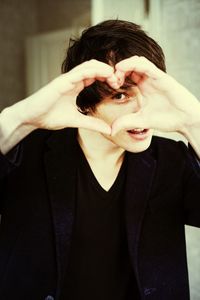 A young man creates a heart shape with hands