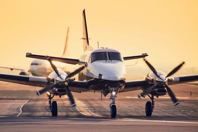 Airplane at airport runway against sky during sunset