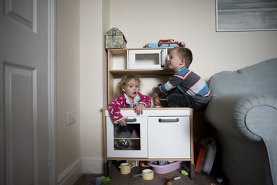 Siblings playing on cabinet by sofa at home