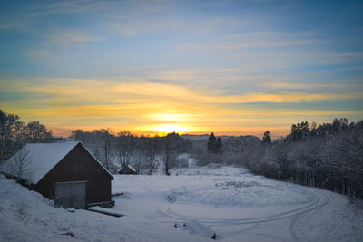 Houses on snow landscape against sky during sunset